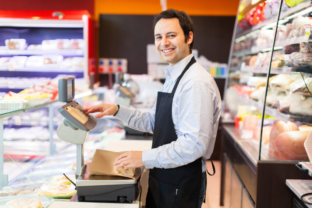 Smiling shop keeper weighing and wrapping deli meats in butcher paper